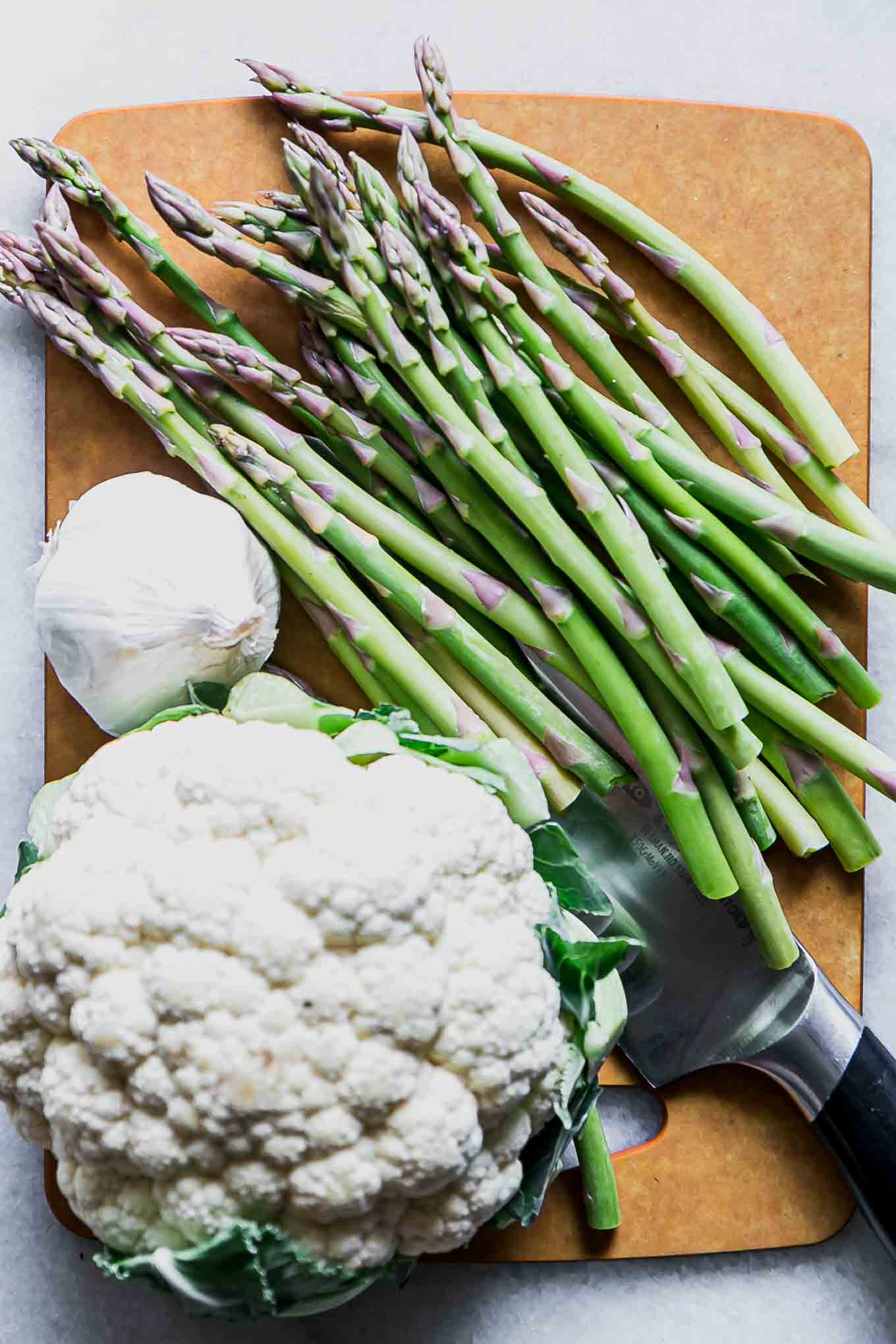 cut asparagus on a wood cutting board with a head of cauliflower