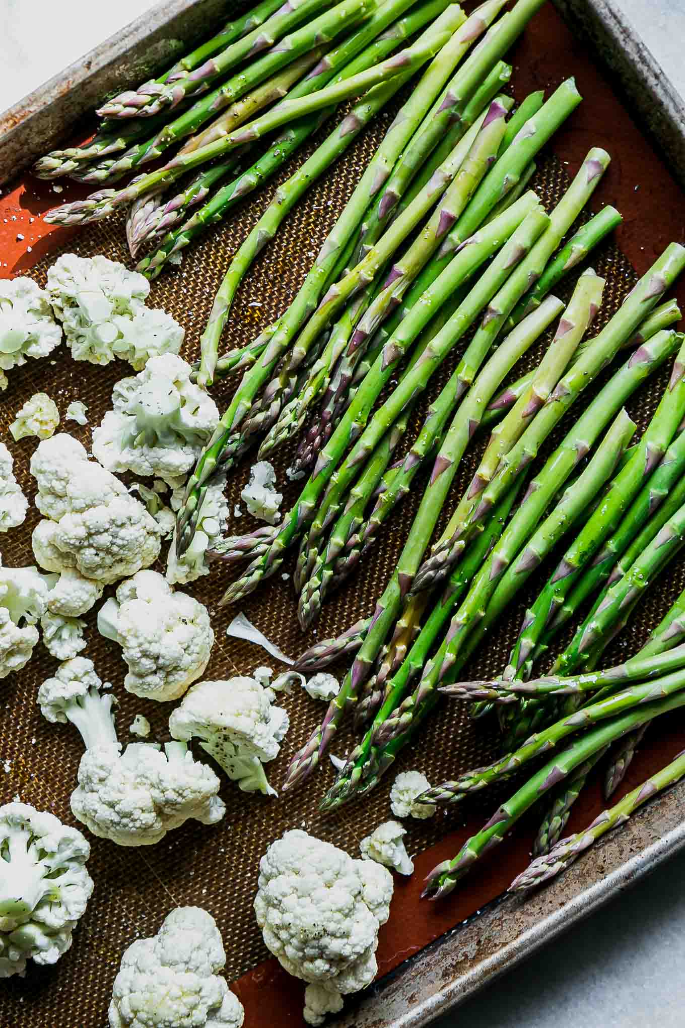 cauliflower florets and asparagus spears on a baking sheet before roasting