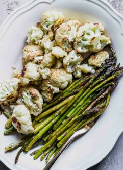 roasted cauliflower and asparagus on a white plate with a gold fork