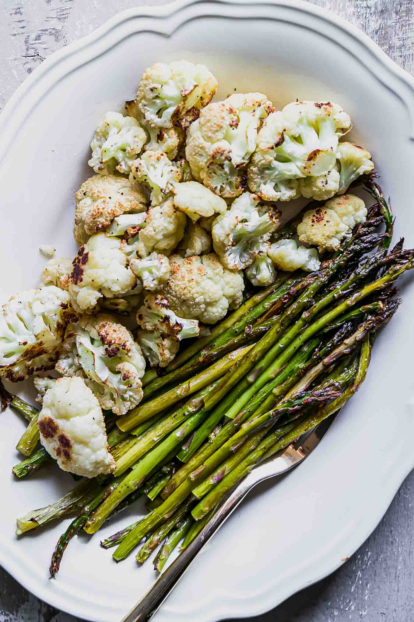 roasted cauliflower and asparagus on a white plate with a gold fork