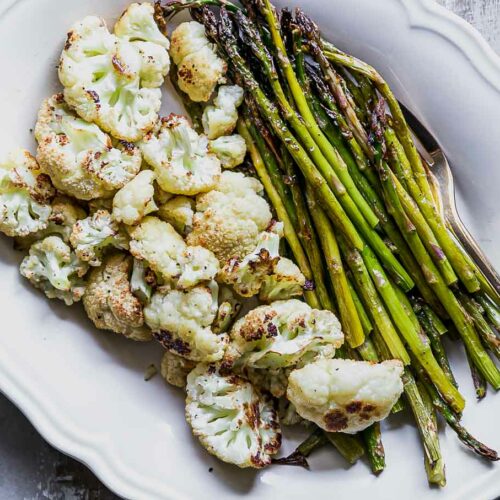 roasted asparagus and cauliflower on a white side dish with a gold fork