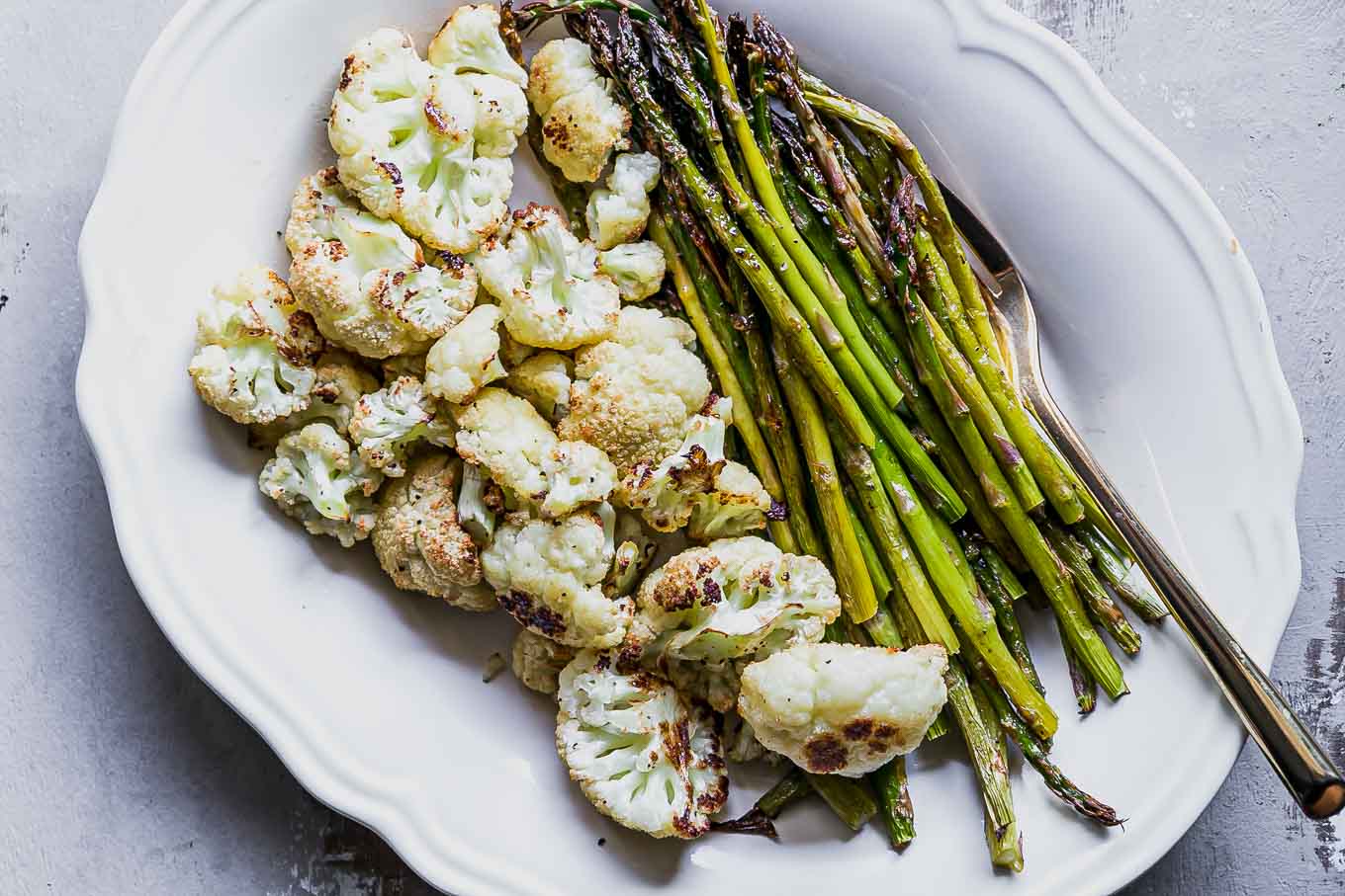roasted asparagus and cauliflower on a white side dish with a gold fork
