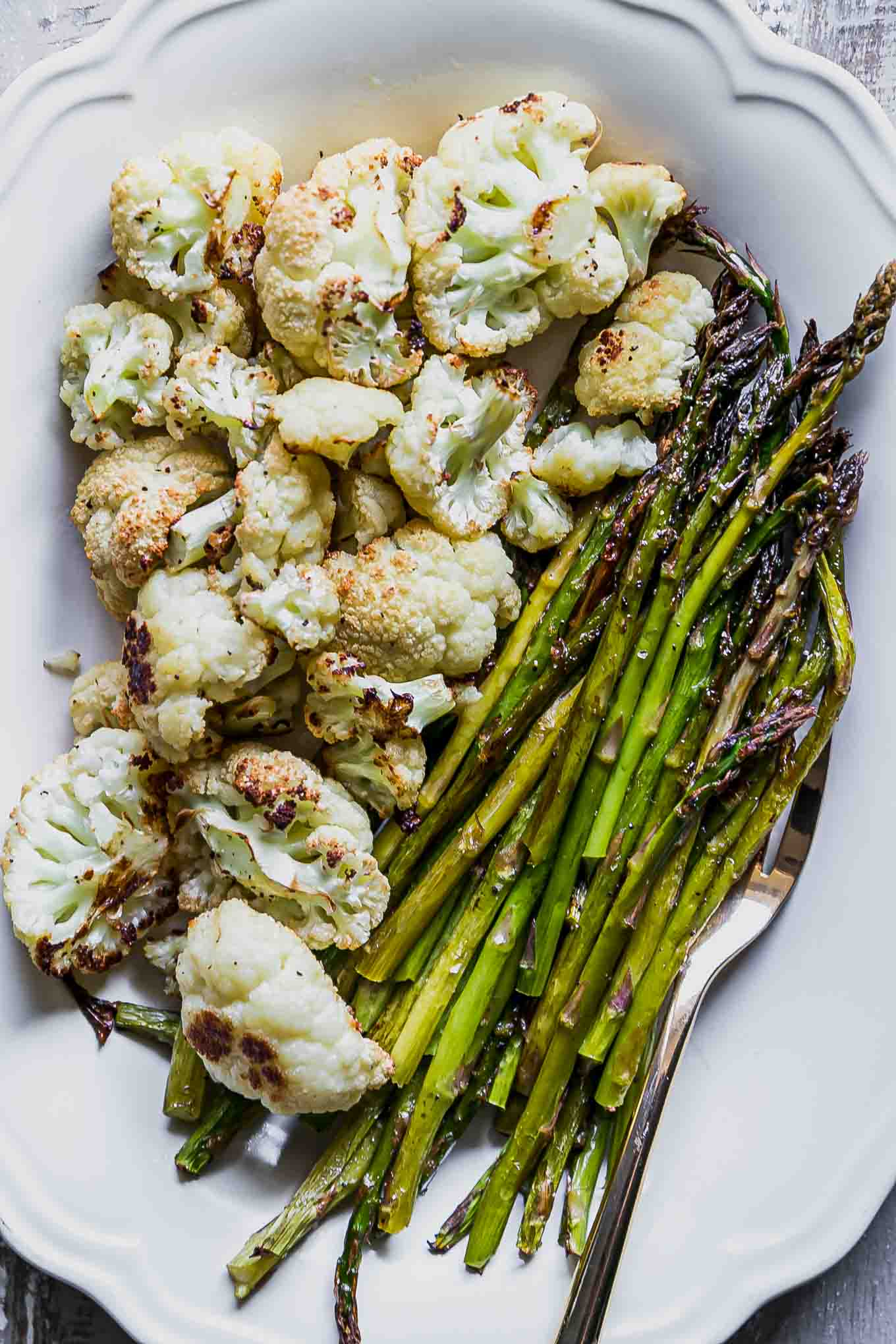 a close up photo of baked cauliflower and asparagus on a white plate