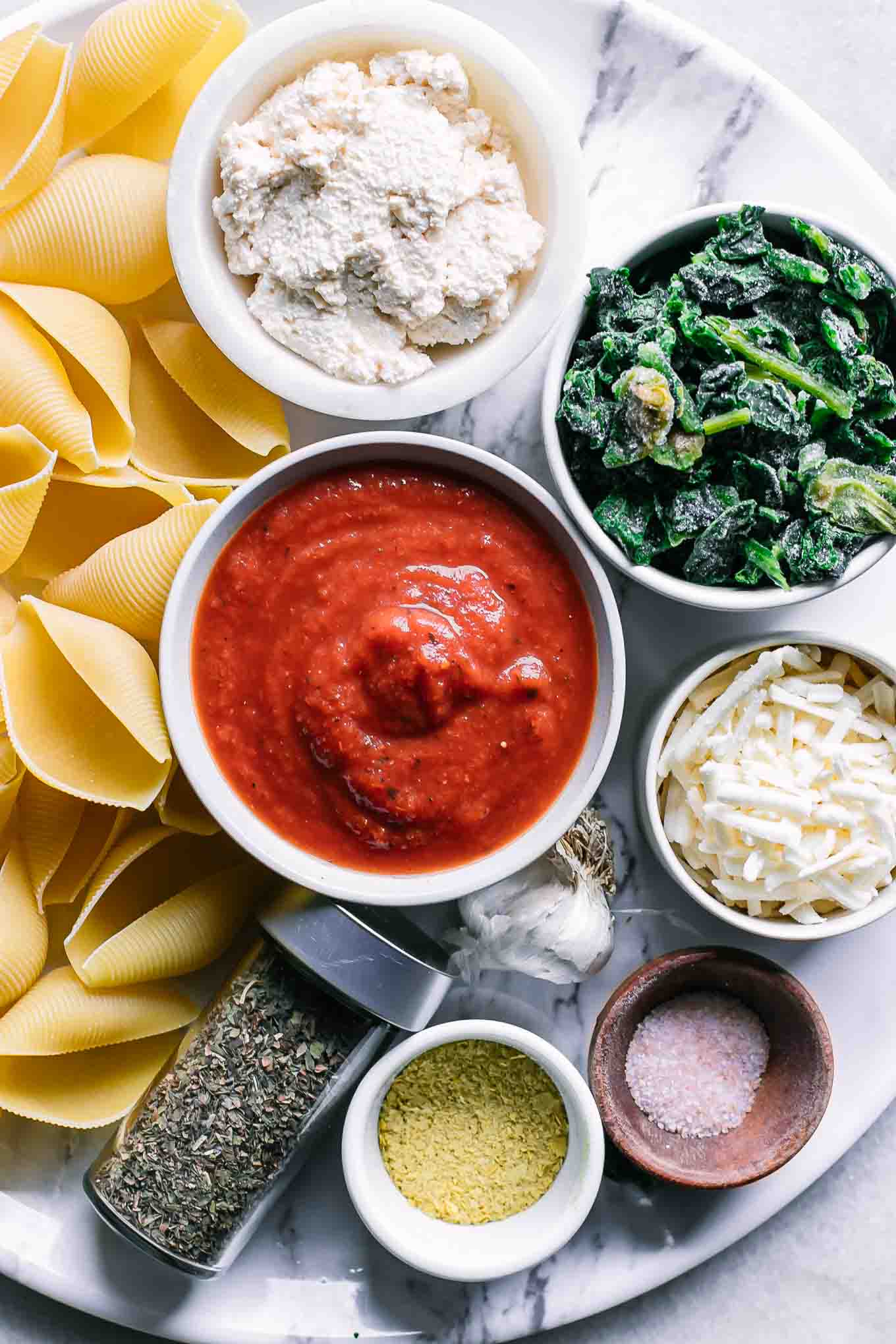 jumbo pasta shells and bowls of vegan ricotta cheese, tomato sauce, spinach, nutritional yeast, and seasonings on a white table