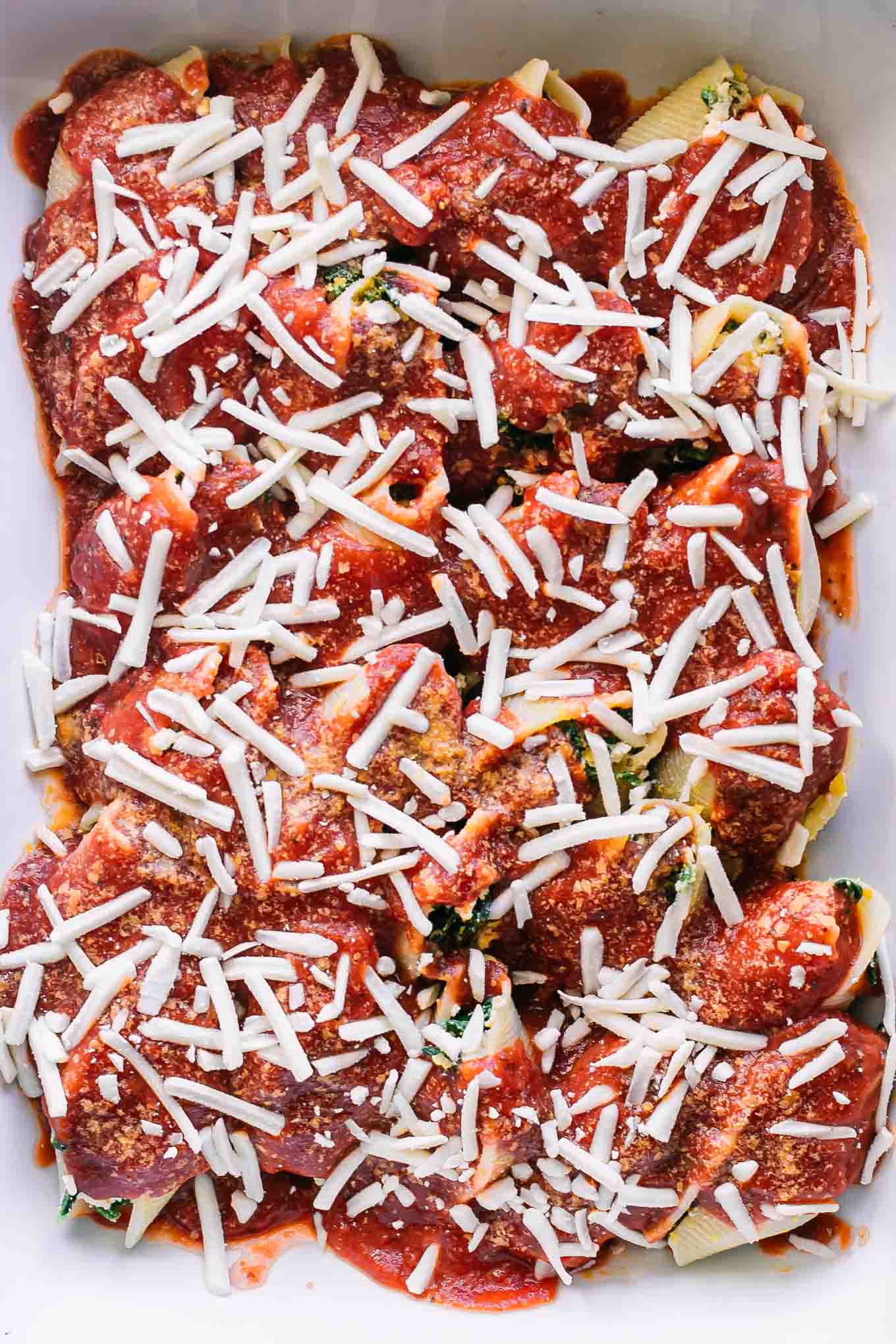 jumbo pasta shells stuffed with plant-based ricotta and spinach and topped with tomato sauce and cheese in a white baking dish