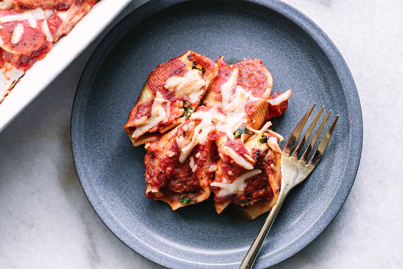 a blue plate with vegan stuffed shells with ricotta and spinach with a gold fork on a white table