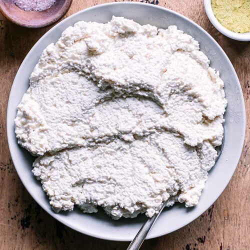 a bowl of tofu ricotta cheese with a gold fork on a wood table