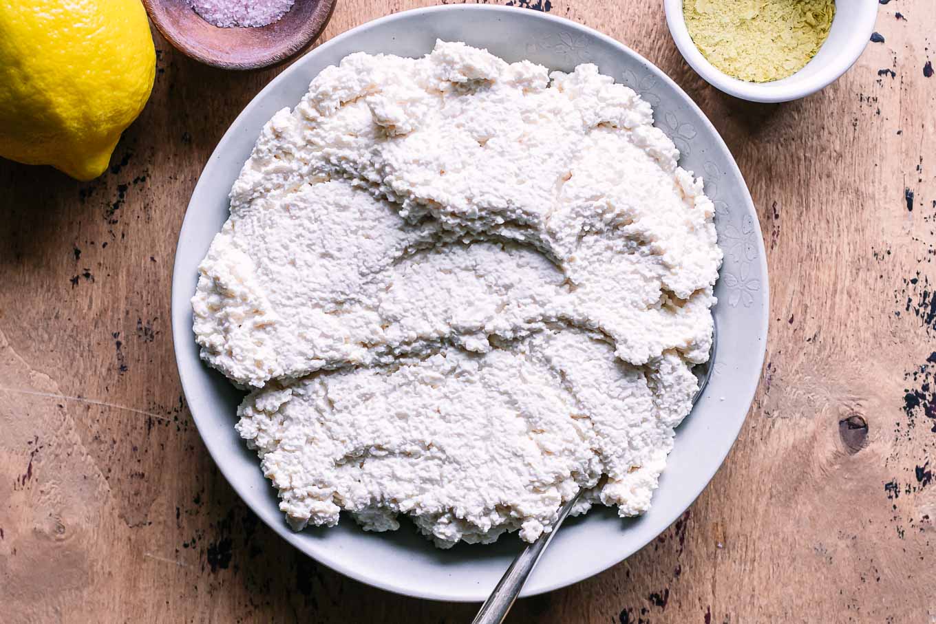 a bowl of tofu ricotta cheese with a gold fork on a wood table