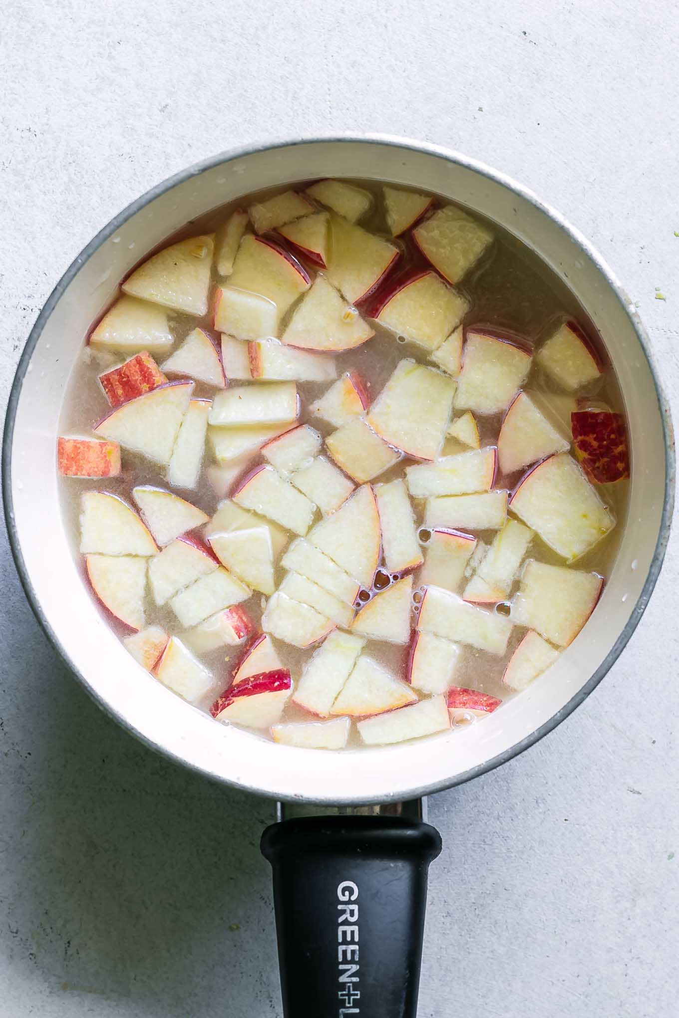 a small pot with oatmeal, sliced apples, and cinnamon sticks before cooking