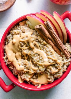 a red bowl with oatmeal cooked with apples and cinnamon on a white table