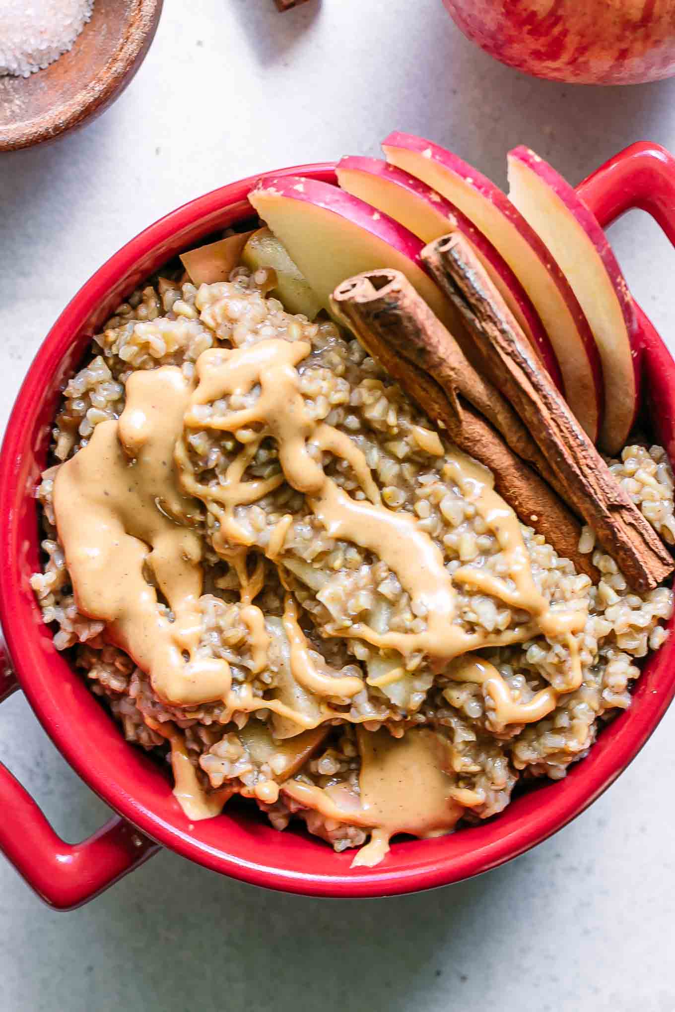 a red bowl with oatmeal cooked with apples and cinnamon on a white table