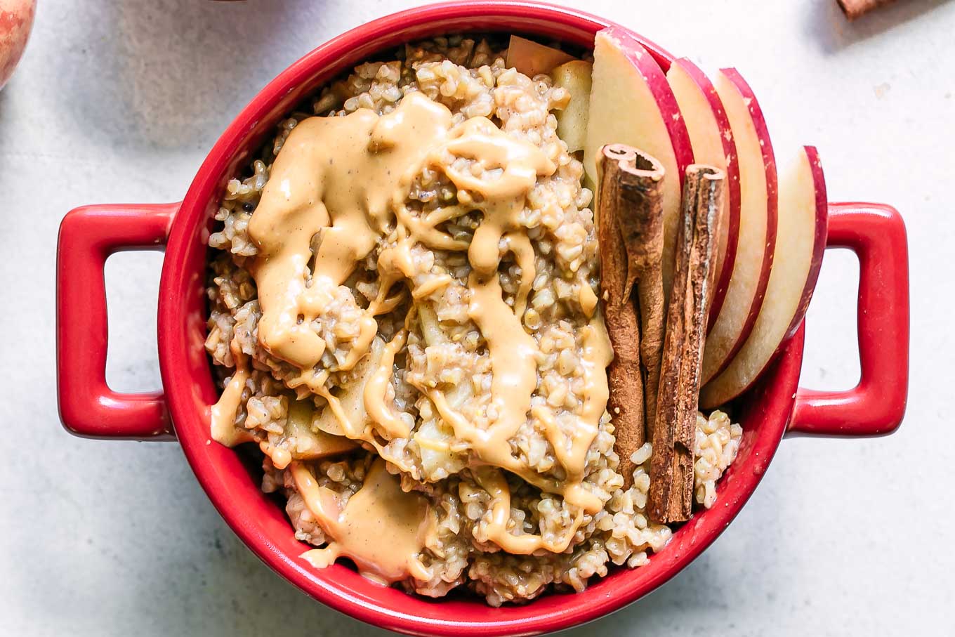 a bowl of oatmeal with apple slices and cinnamon sticks on a white table