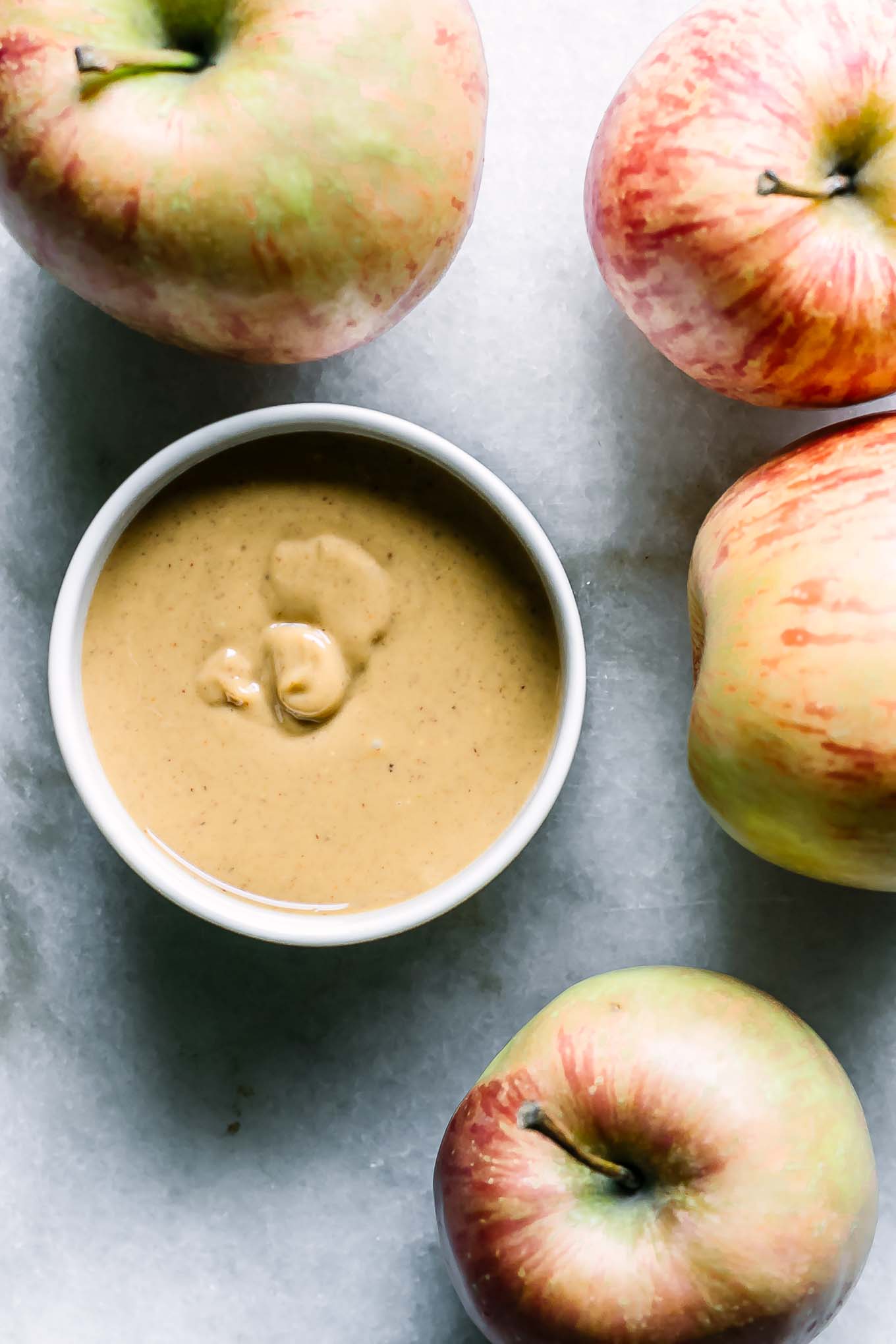 a bowl of peanut butter on a table with four red apples