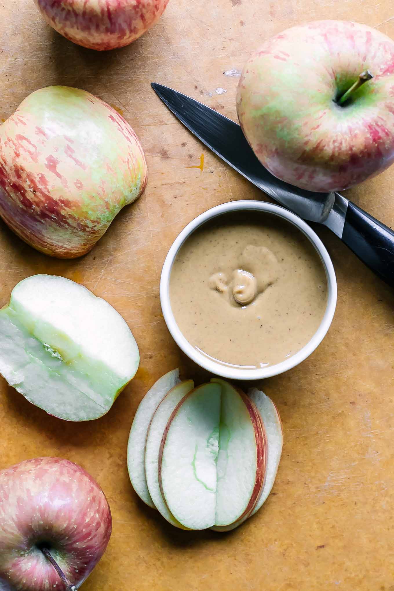 sliced apples on a woo cutting board with a knife and a bowl of peanut butter