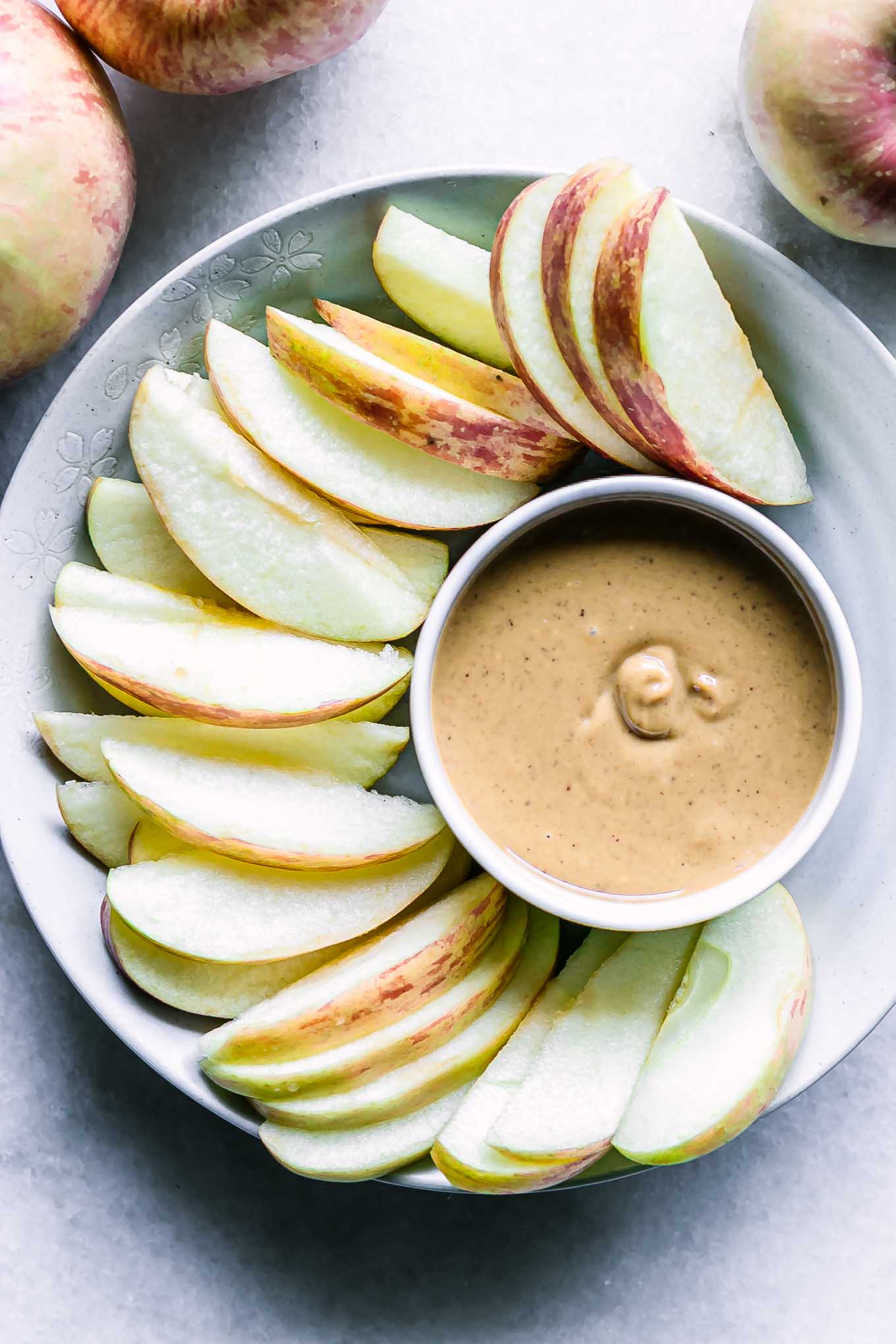 a bowl with peanut butter and apple slices on a white table with apples