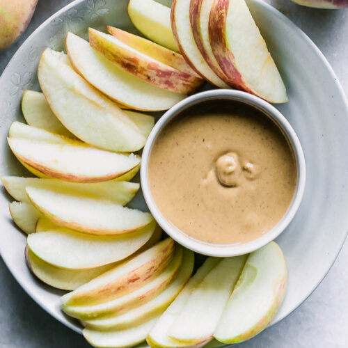 a bowl with peanut butter and apple slices on a white table