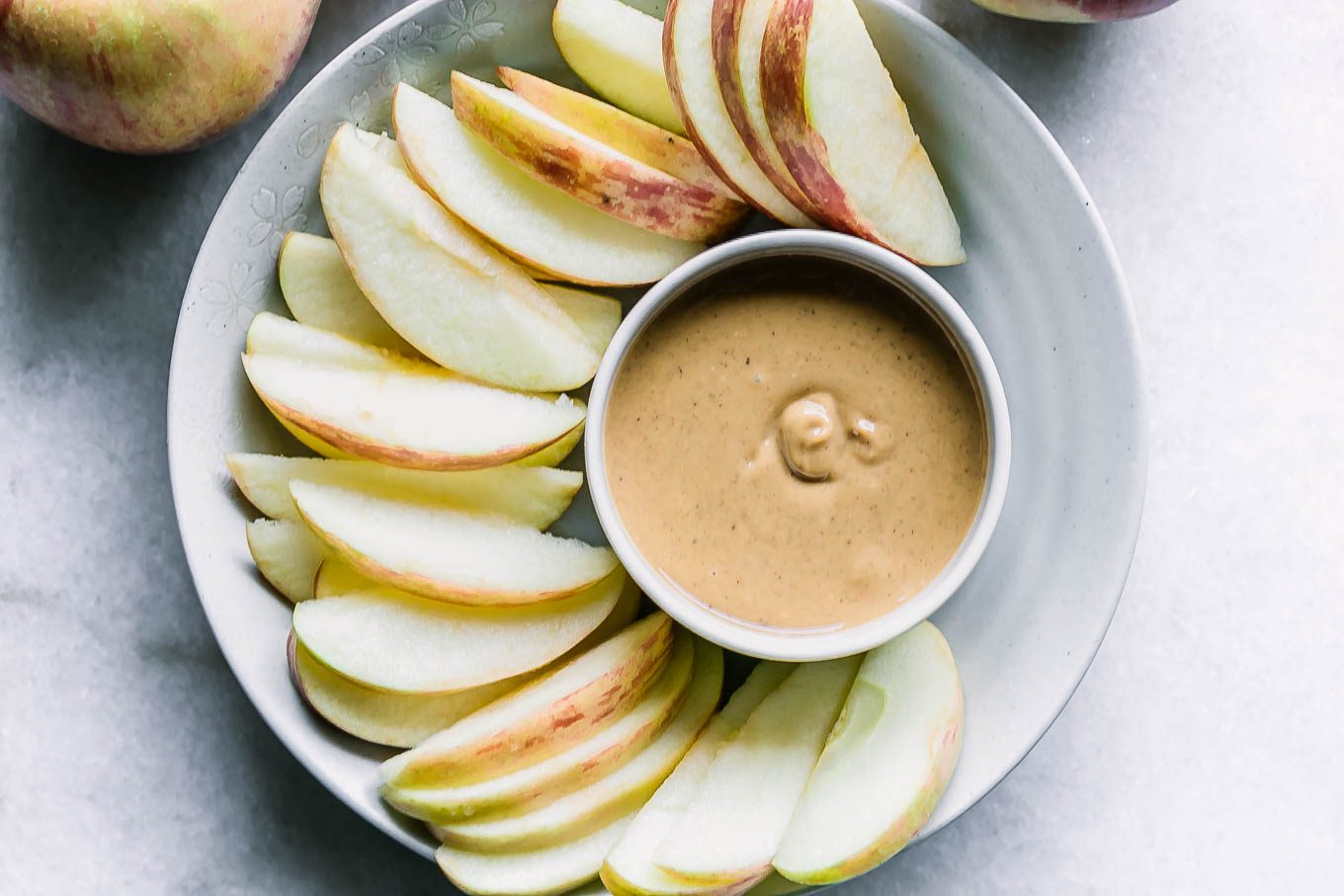 a bowl with peanut butter and apple slices on a white table