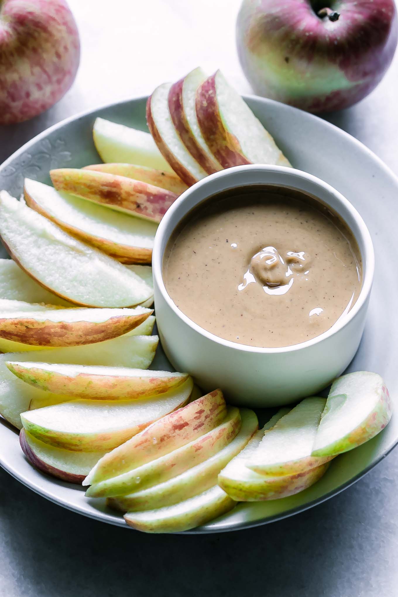 a white plate with sliced apples and a small bowl of peanut butter