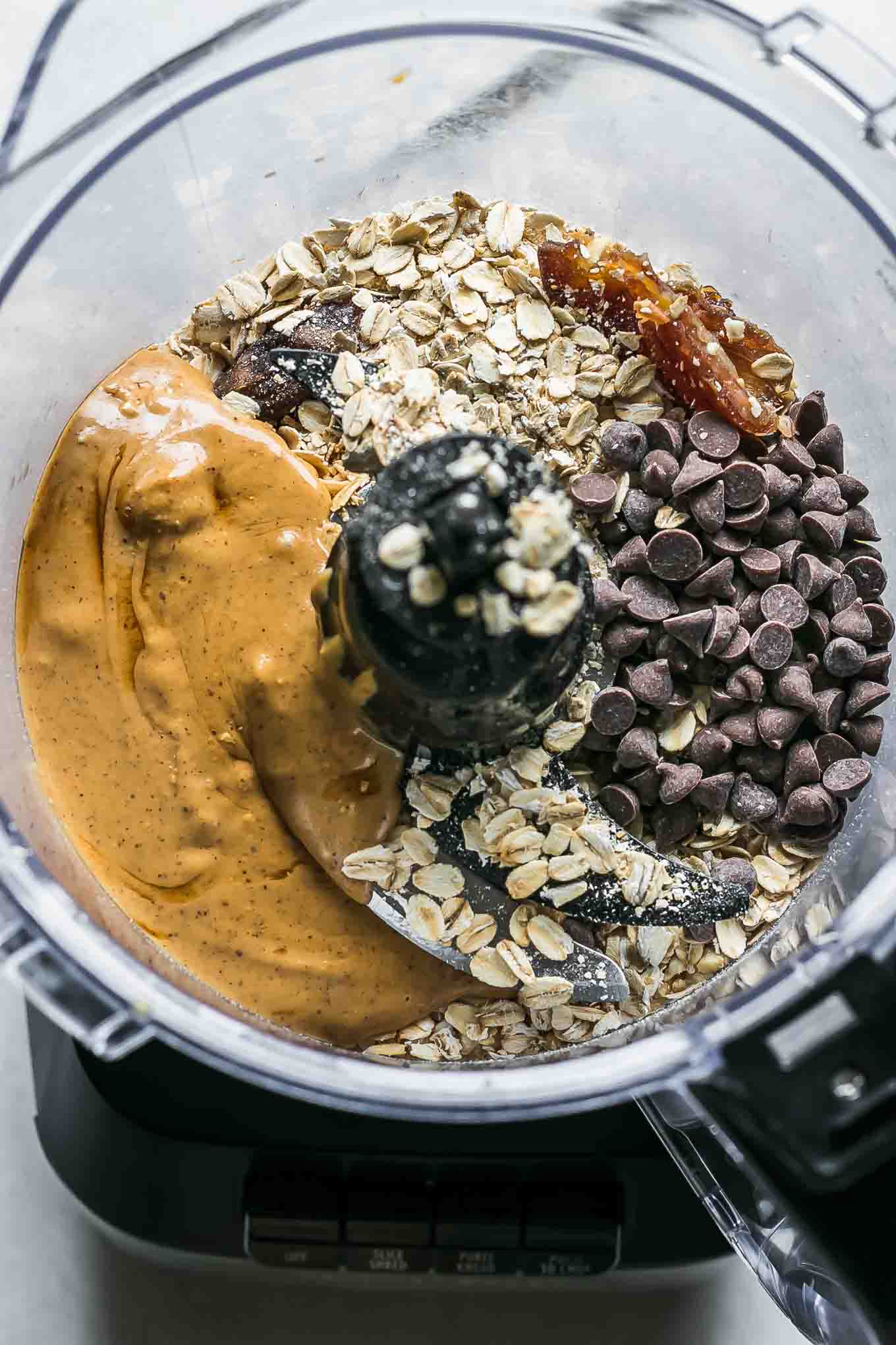 a food processor with oats, dates, chocolate chips, peanuts, and peanut butter inside