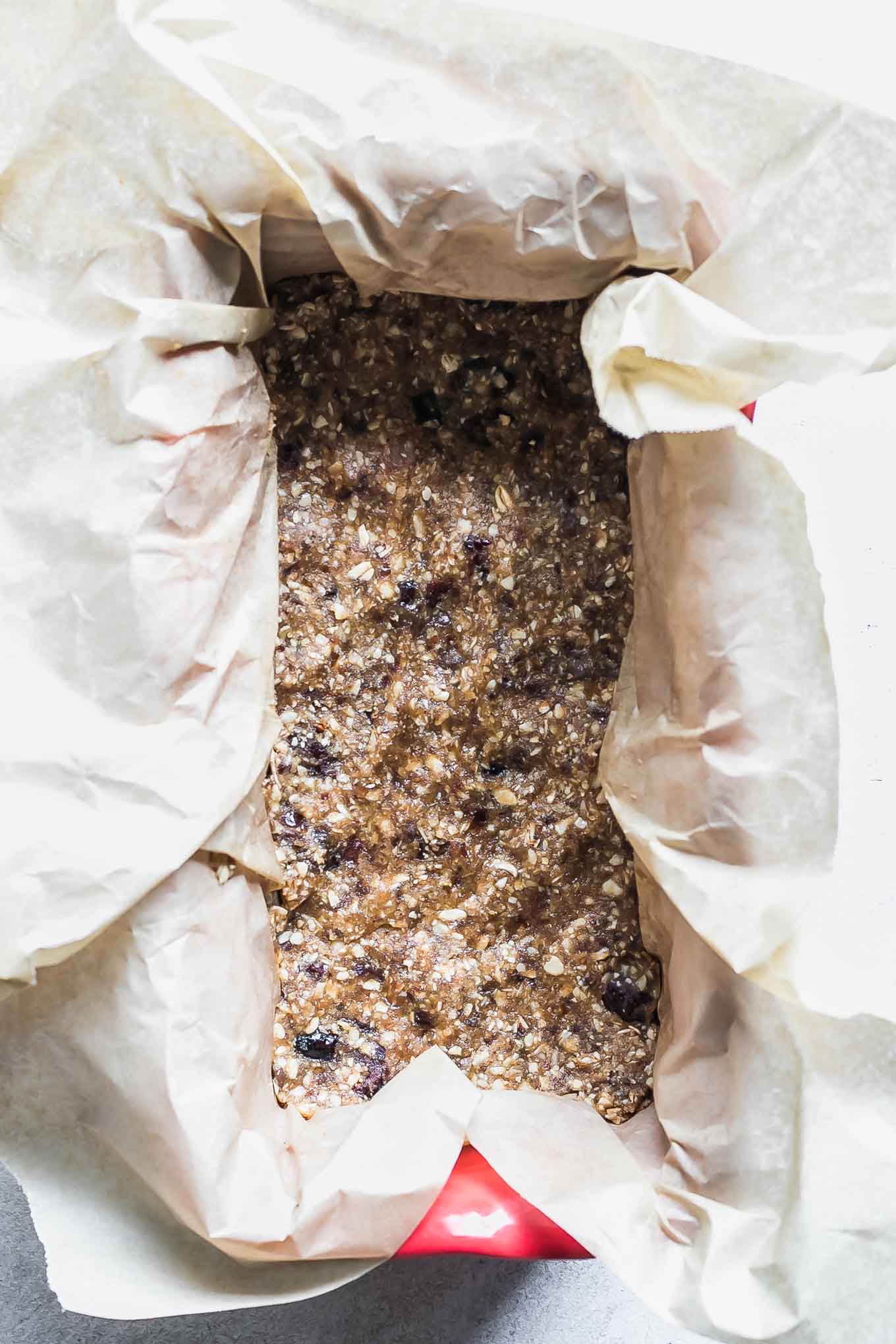 a loaf pan with parchment paper and granola bar ingredients inside on a white table
