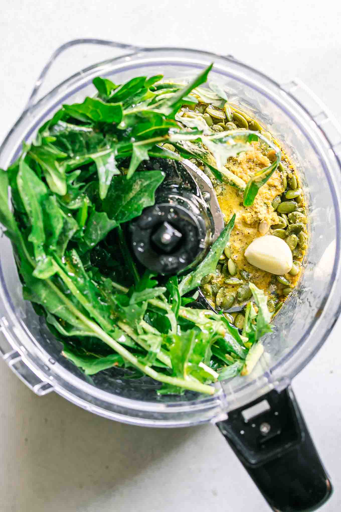 dandelion greens inside a food processor with pesto ingredients