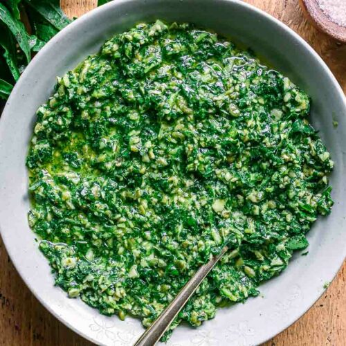 a bowl of dandelion leaves pesto sauce on a wood table with fresh dandelion greens