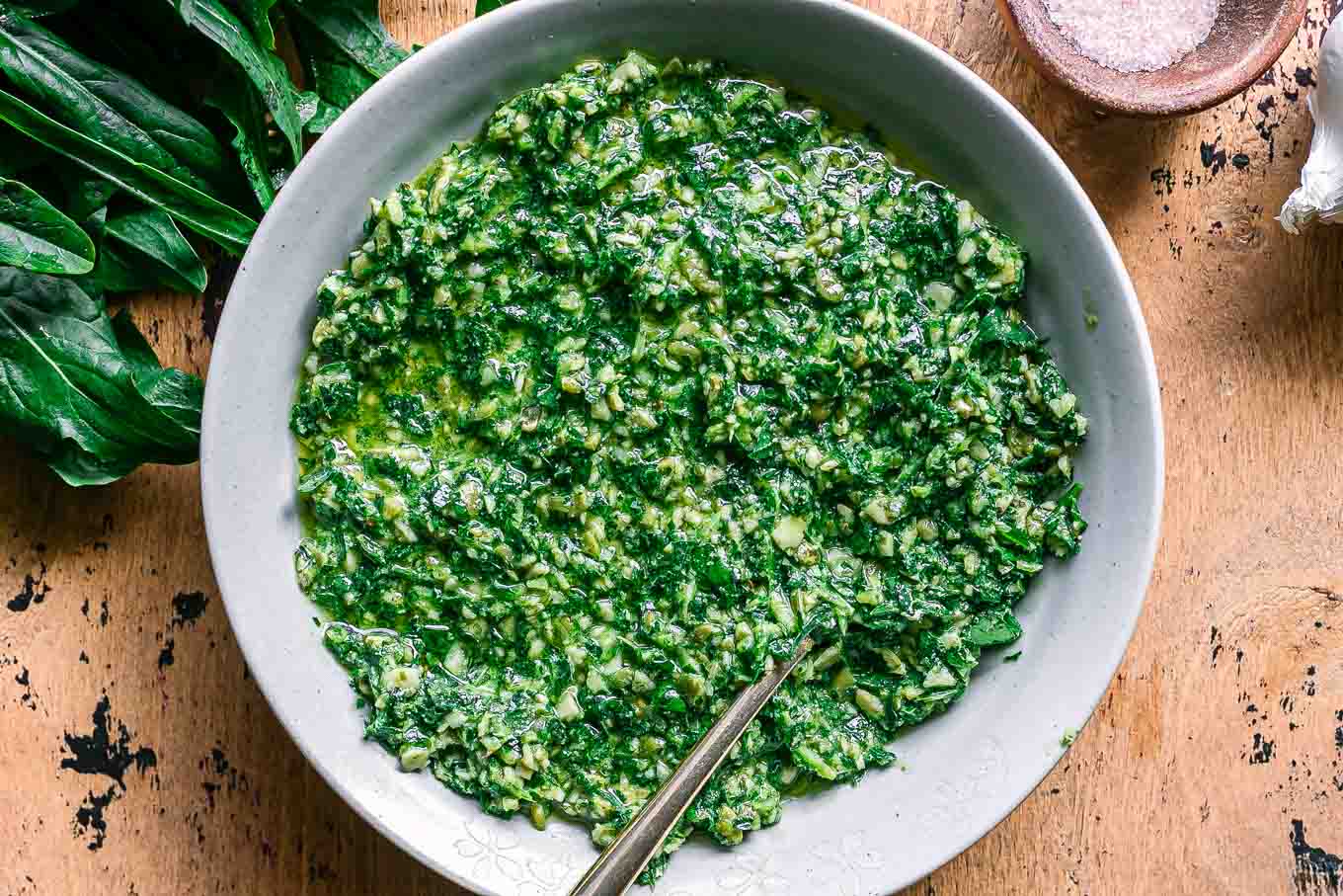 a bowl of dandelion leaves pesto sauce on a wood table with fresh dandelion greens