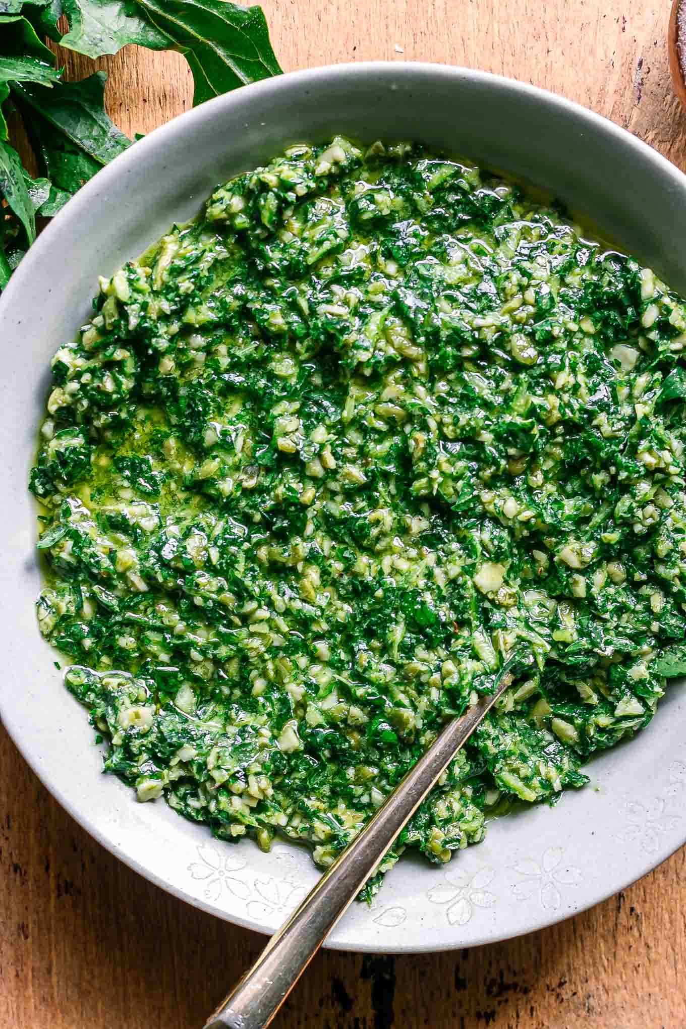 a bowl of green dandelion pesto sauce on a wood table