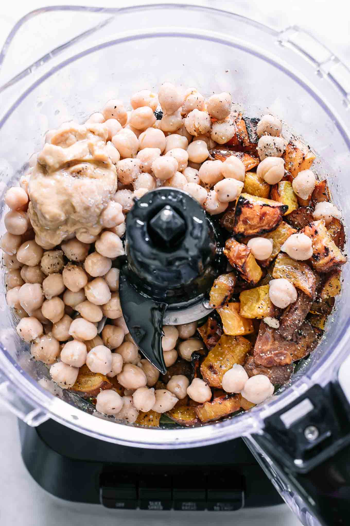 a food processor with chickpeas, roasted golden beets, tahini, oil, garlic, salt and pepper before blending