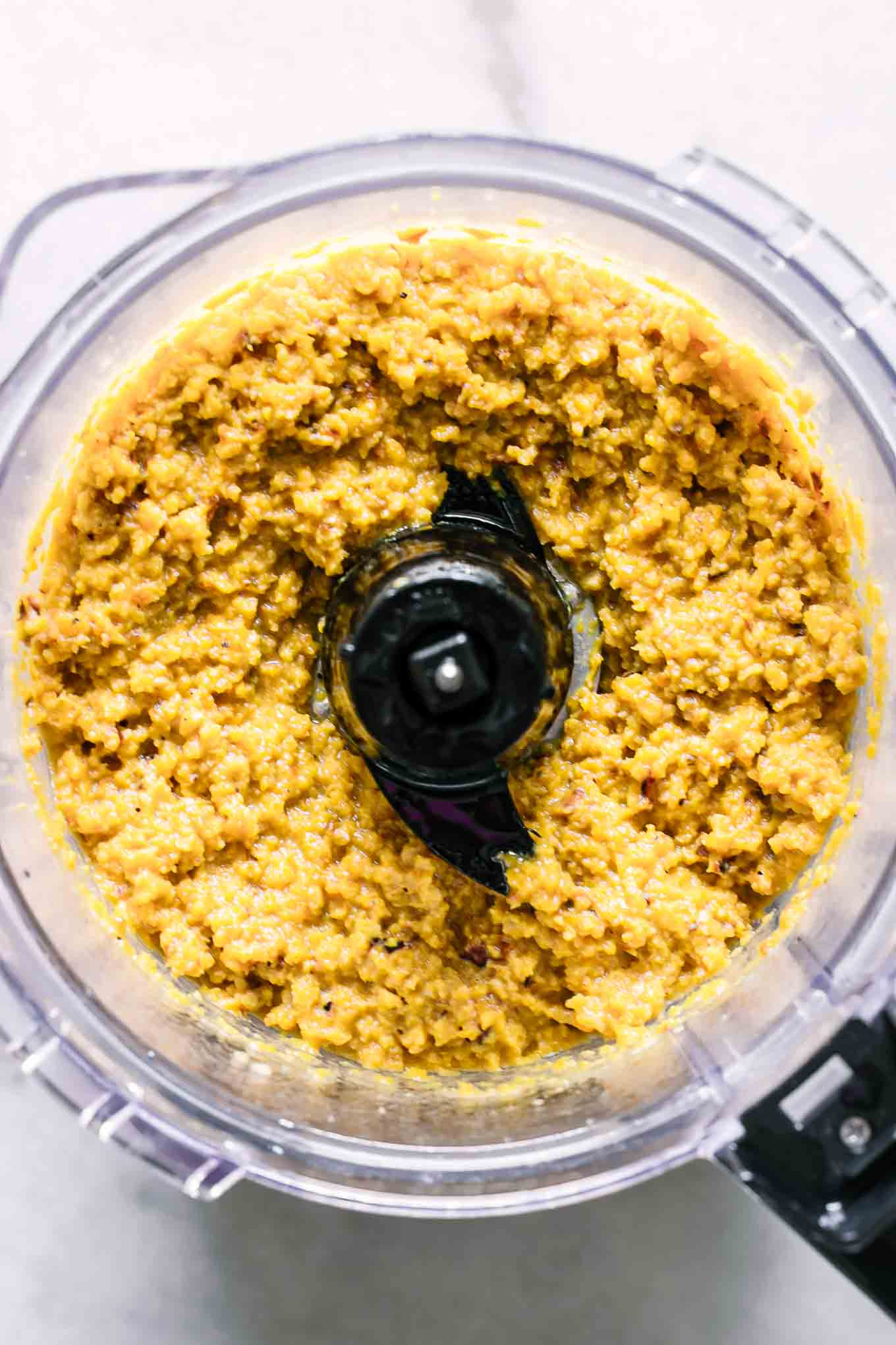 a food processor with blended golden beet hummus inside