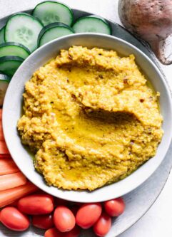 a bowl of hummus made with golden beets on a plate with cut vegetables for dipping