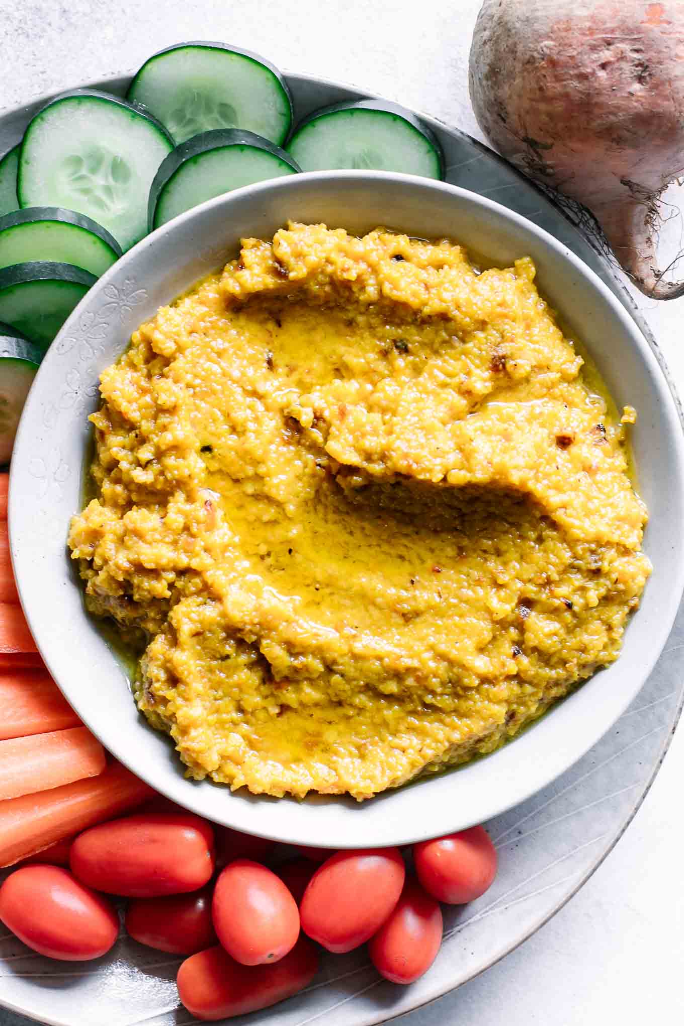 a bowl of hummus made with golden beets on a plate with cut vegetables for dipping