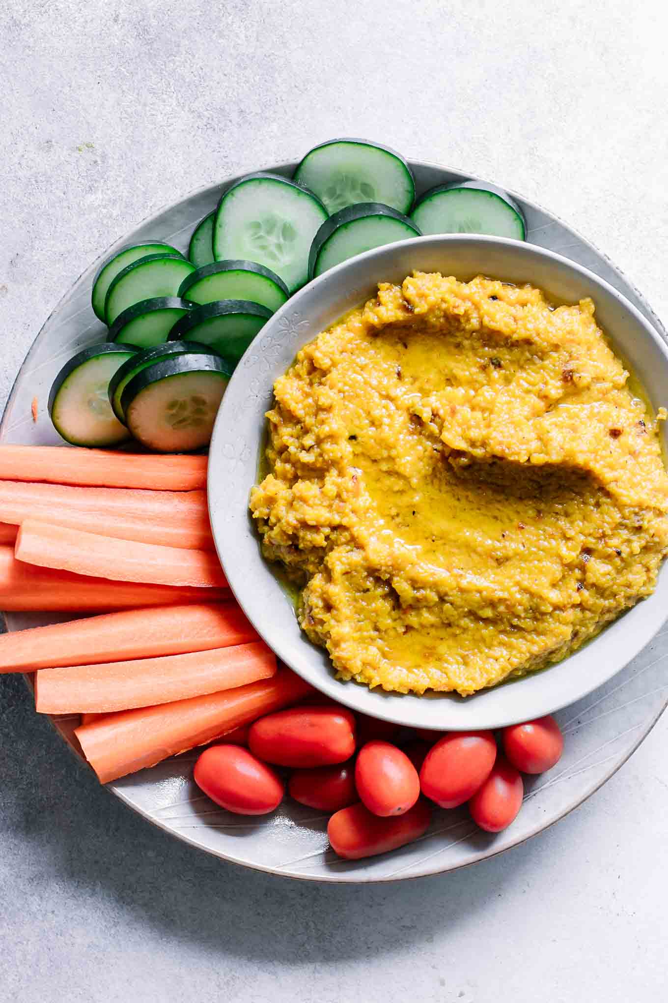 a plate with orange golden beet hummus dip with cut carrots, cucumbers, and cherry tomatoes