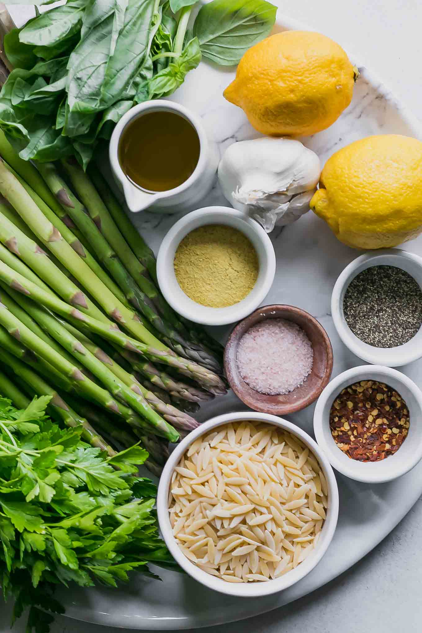 asparagus, basil, parsley, lemons, garlic, and bowls of orzo and seasonings for orzo pasta