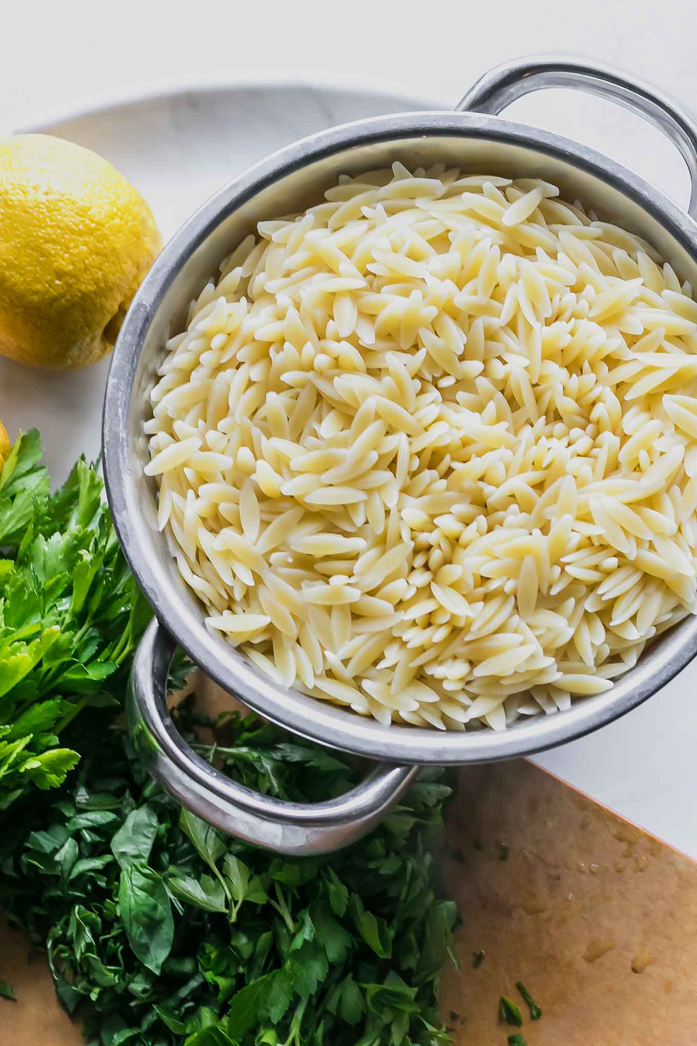 a colander with orzo on a table with fresh herbs