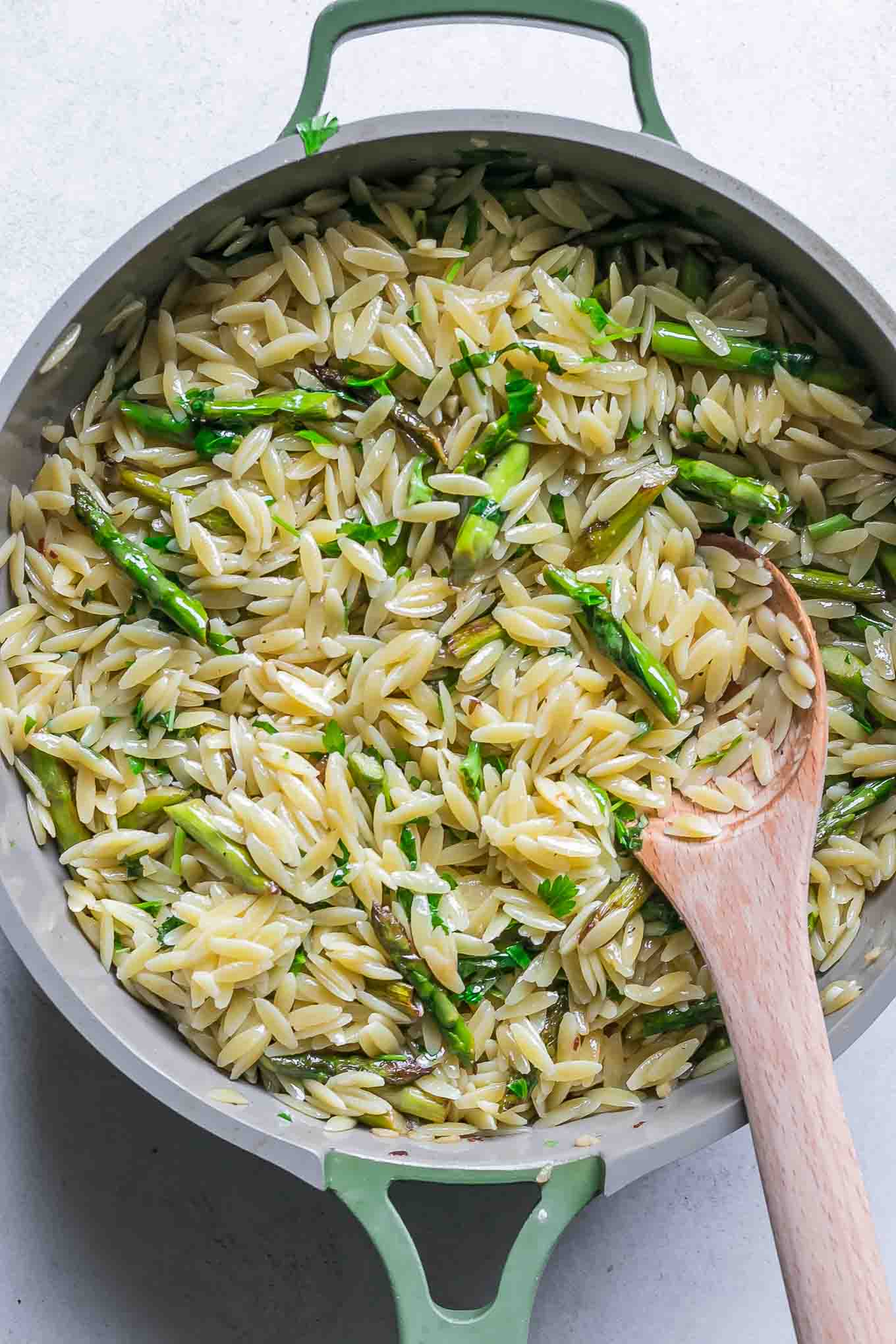 a pan with orzo and asparagus pasta with a wooden spoon