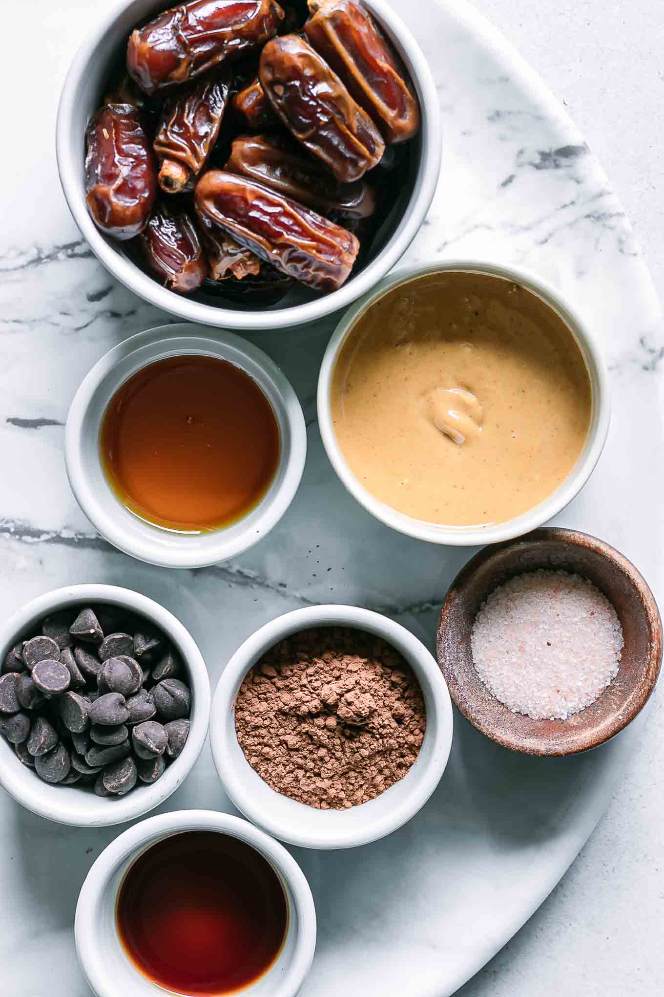 bowls of dates, nut butter, chocolate chips, cocoa powder, and seasonings for brownie bites