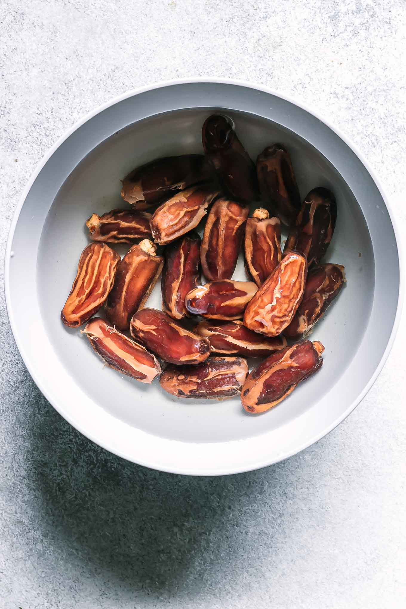 a bowl of dates soaking in hot water on a white table