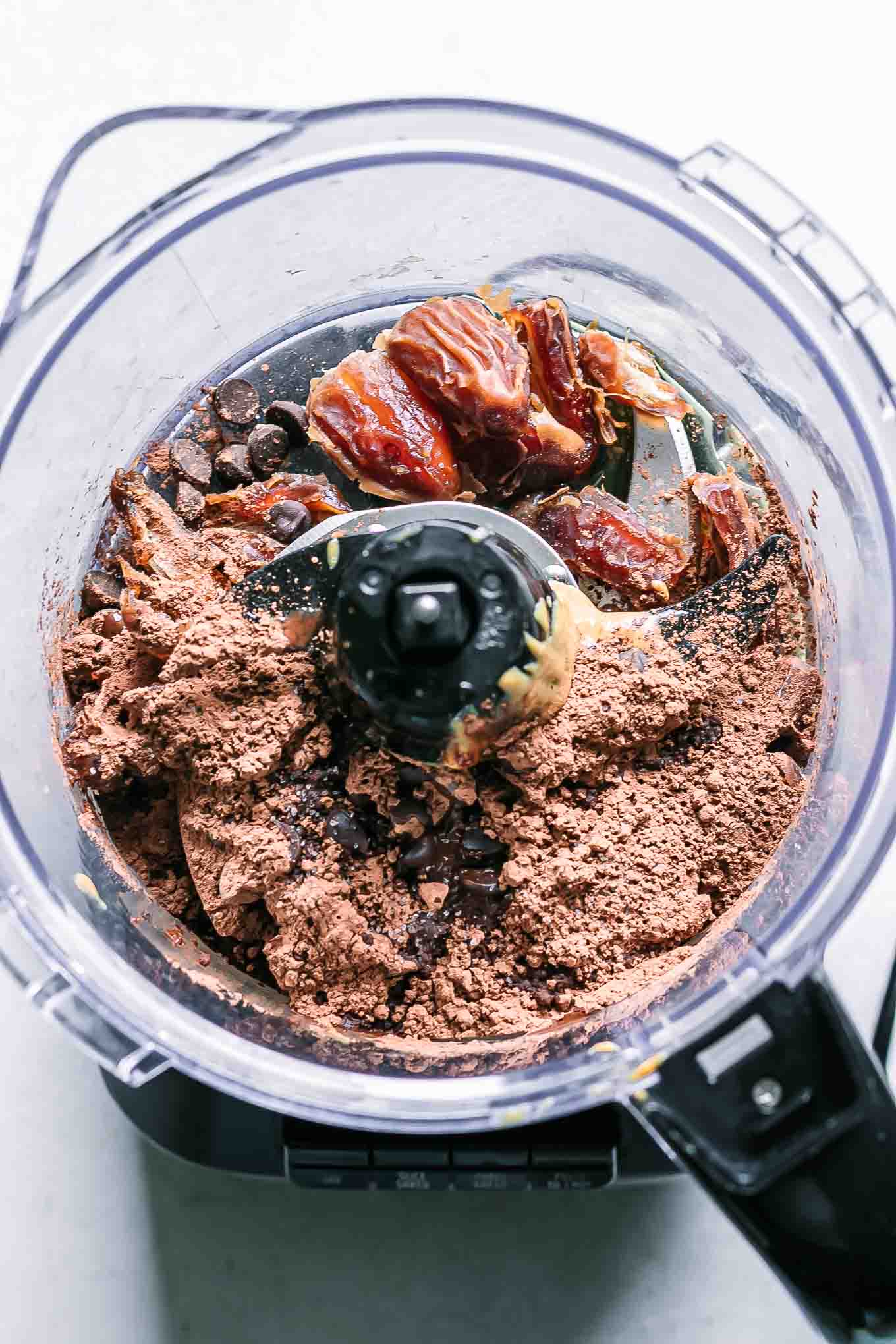 a food processor filled with dates, cocoa powder, chocolate chips, and other ingredients for brownie balls