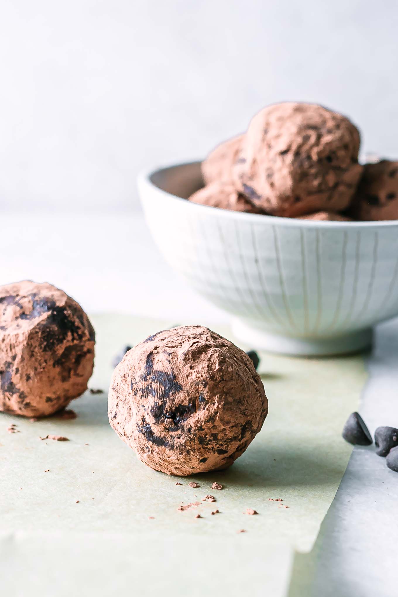 a chocolate brownie bite ball on a white table with a bowl of more snack balls in the background