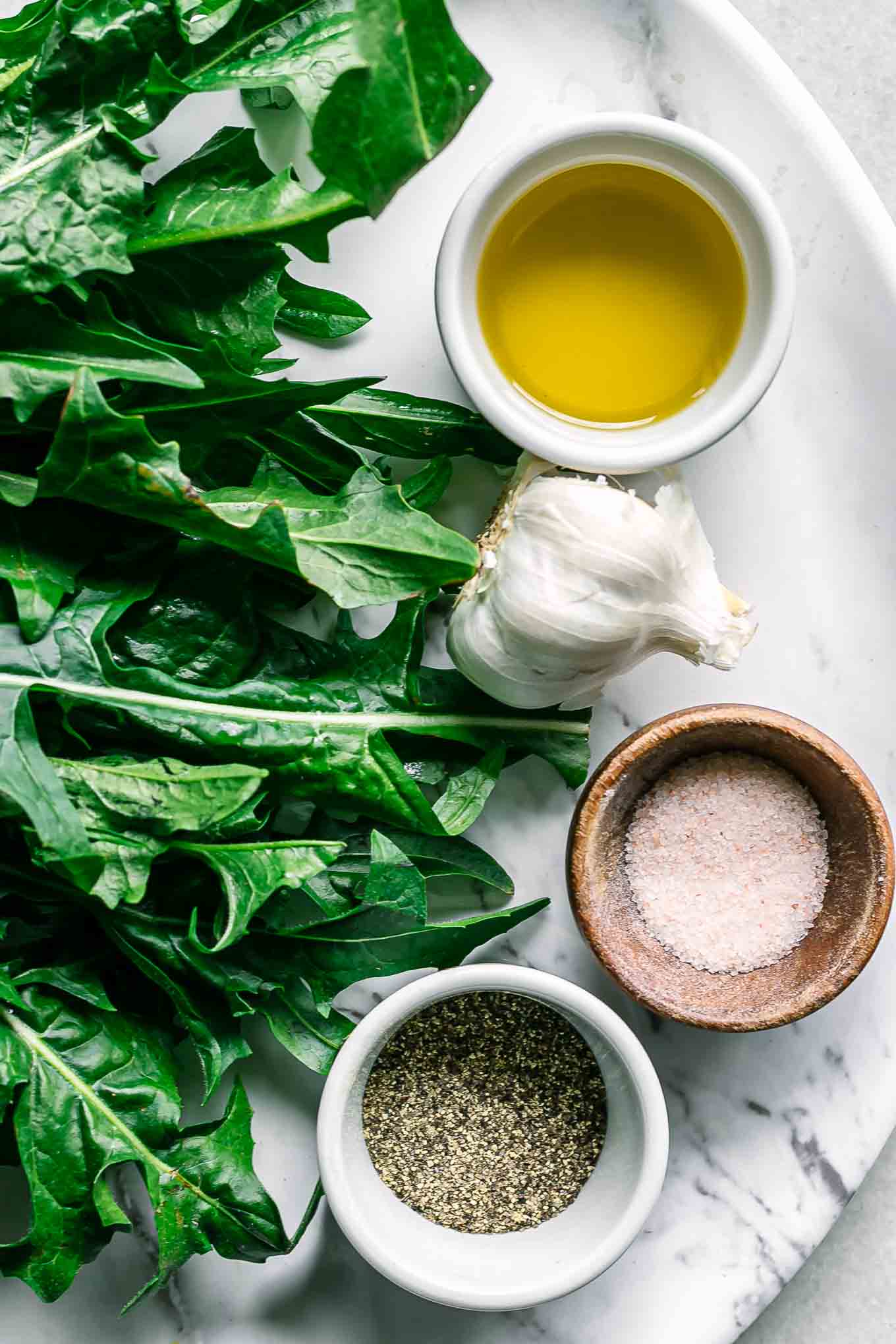 dandelion leaves and bowls of oil, salt, pepper, and red pepper on a white table