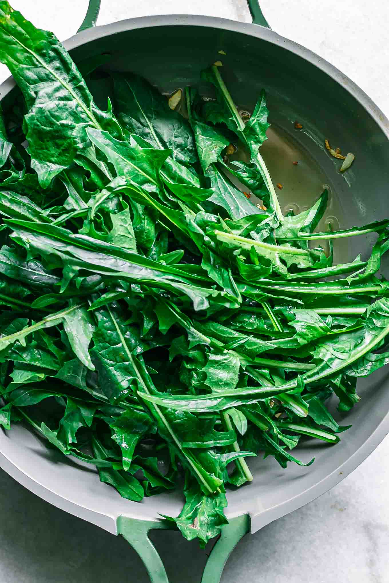 raw dandelion greens in a pan with oil and garlic