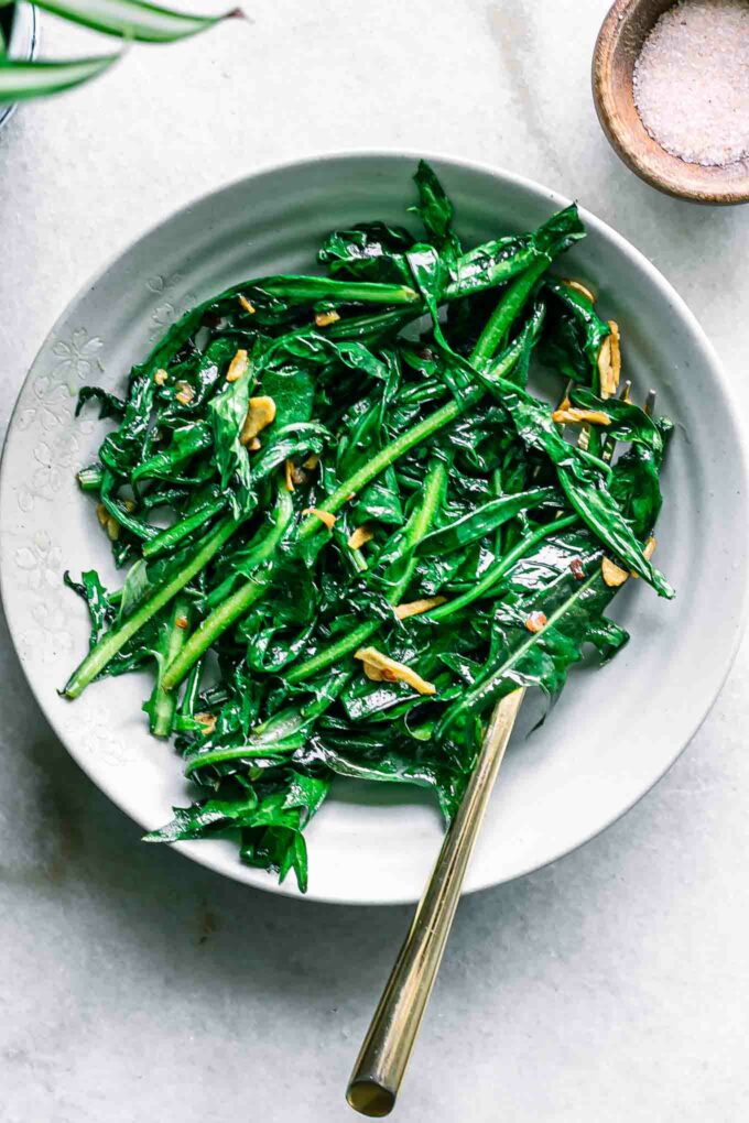 a white bowl with sauteed dandelion greens and a gold fork on a white table