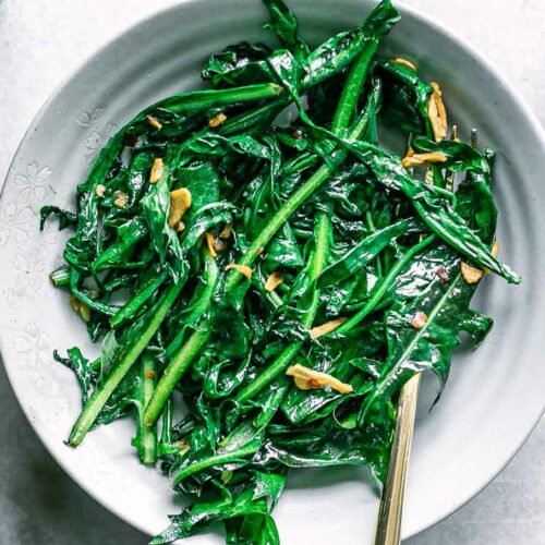 sautéed dandelion leaves in a white bowl with a gold fork on a white table