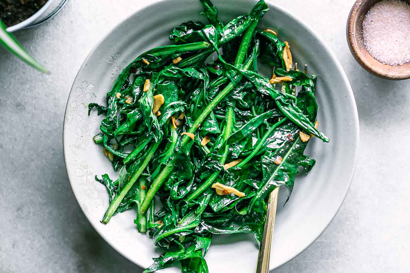 sautéed dandelion leaves in a white bowl with a gold fork on a white table