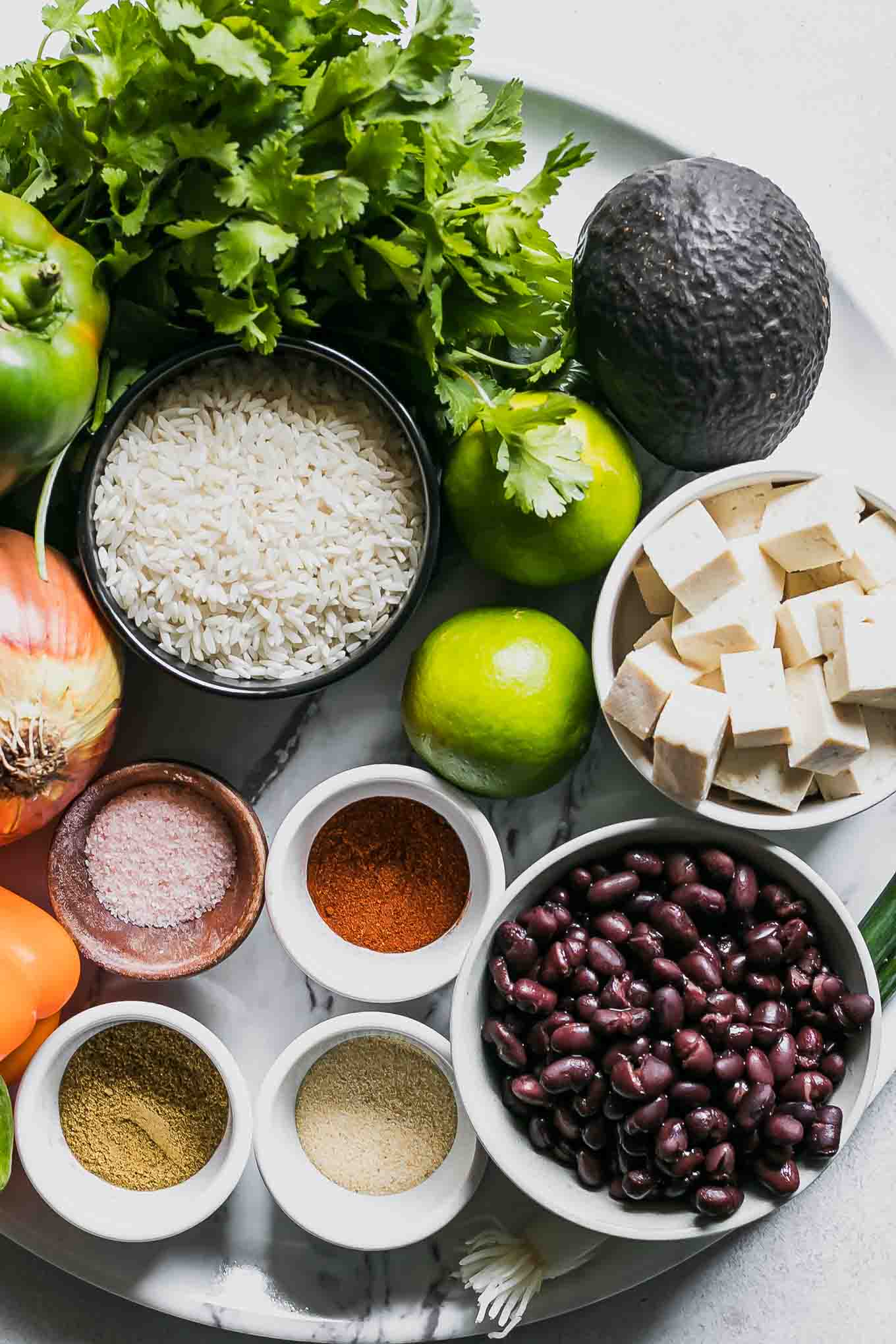 tofu, black beans, avocado, limes, and bowls of rice, seasonings, and fresh cilantro for a fajita bowl