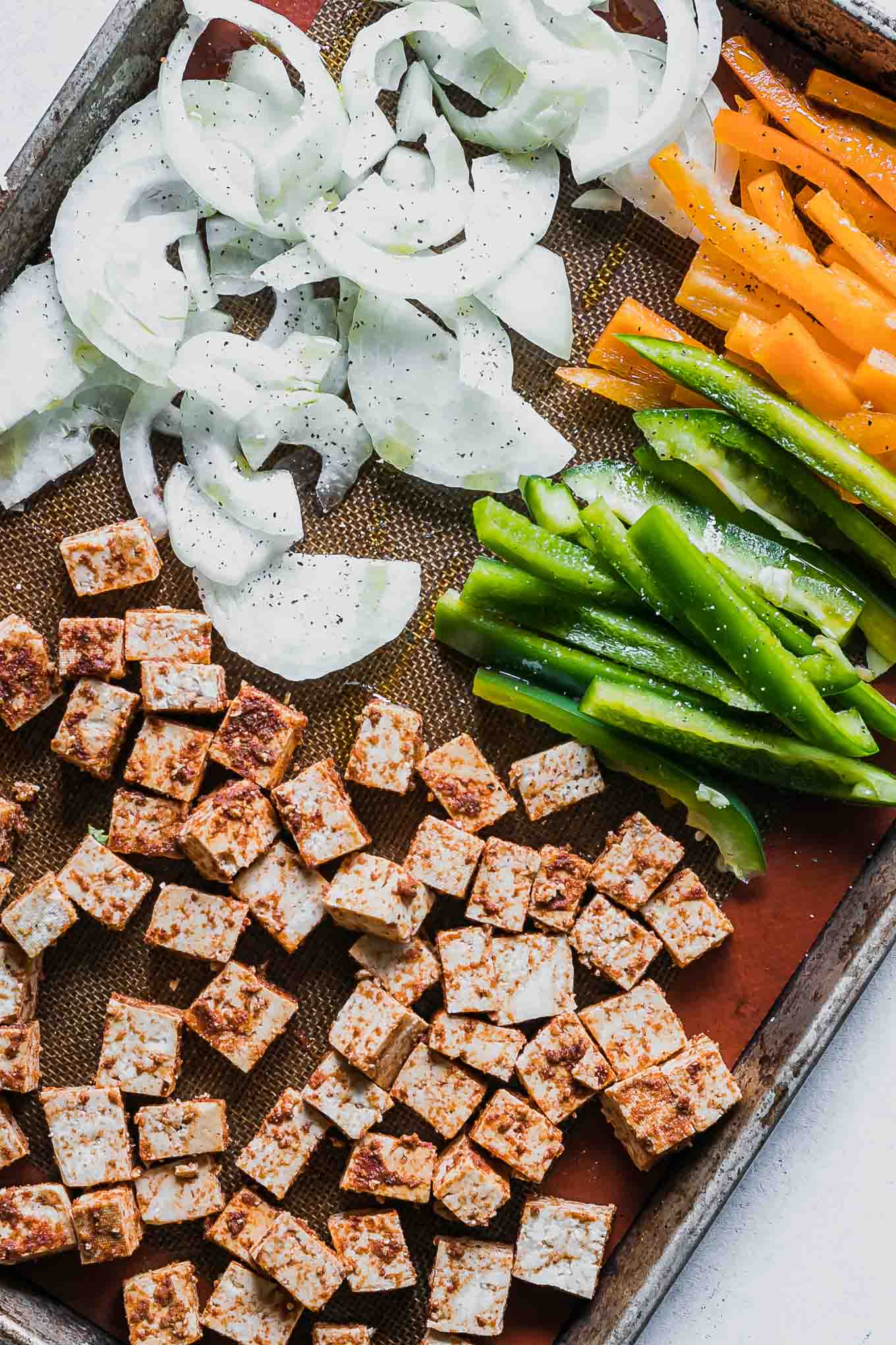 a sheet pan with seasoned tofu and sliced onions with bell peppers before roasting