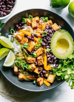 a tofu, vegetable, and rice fajita bowl with black beans, limes, and avocado on a white table