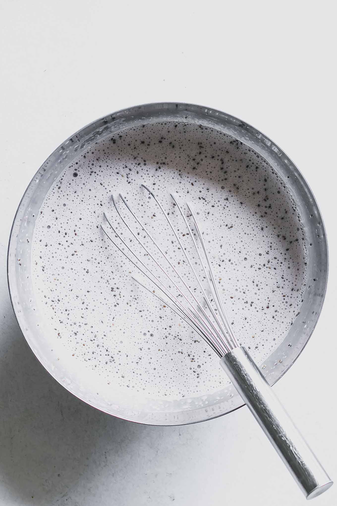 a mixing bowl with milk and chia seeds and a whisk on a white table