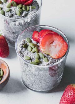 a glass with strawberry chia seed pudding and topped with a sliced strawberry on a white table with fresh strawberries
